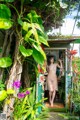 A woman standing in the doorway of a house surrounded by plants.