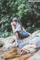 A woman sitting on a rock in a stream.