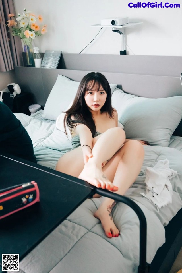 A woman sitting on top of a bed next to a table.