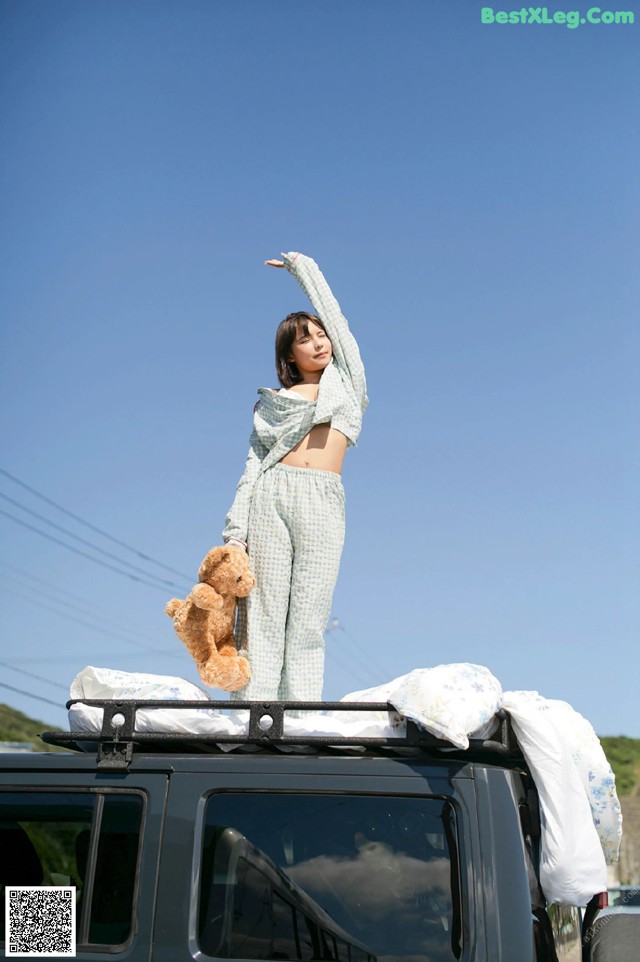 A woman standing on top of a car holding a teddy bear.