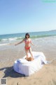 A woman in a red bikini standing on a bed on the beach.