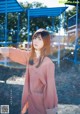 A woman in a pink shirt is standing in front of a playground.