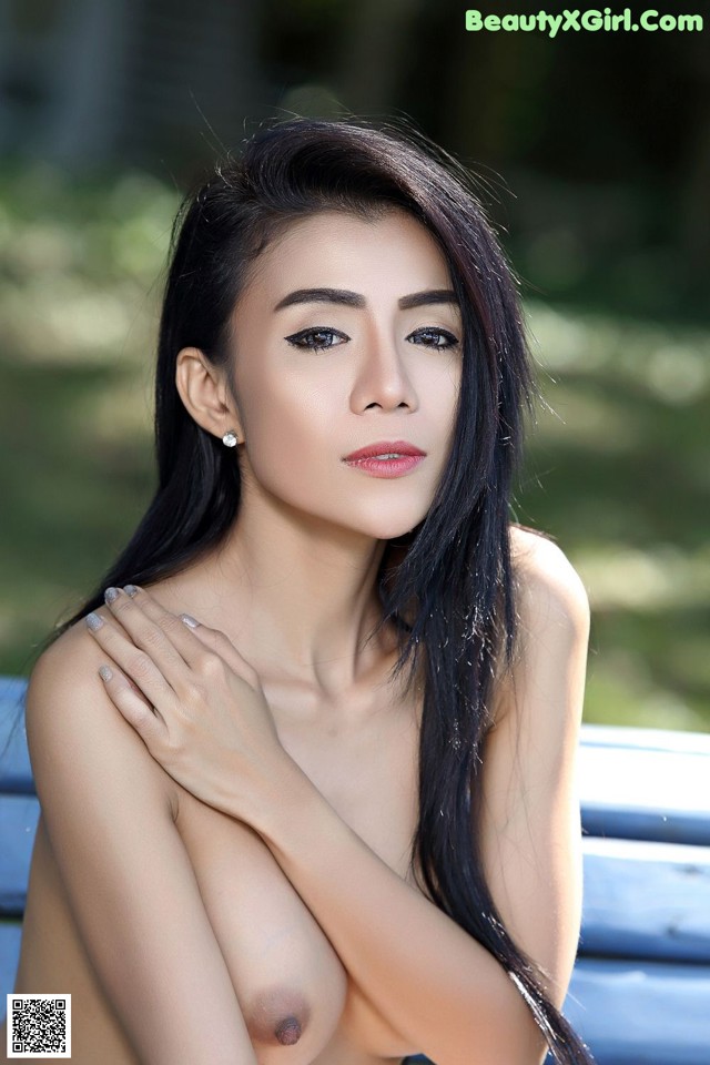 A naked asian woman posing in front of a blue car.