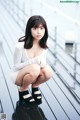 A woman in a white shirt and black sandals crouching on a wooden floor.