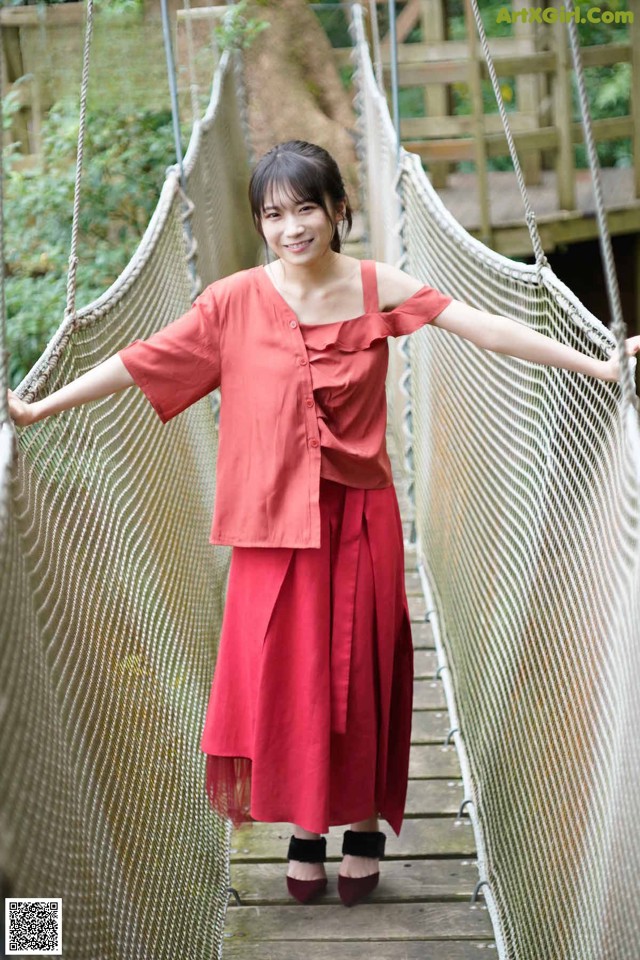 A woman in a red dress standing on a rope bridge.