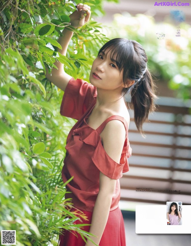 A woman in a red dress leaning against a tree.
