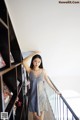 A woman in a blue dress standing next to a book shelf.